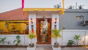 A building entrance with a wooden door, potted plants, and a yellow awning. - Pi Karya Beach (Penida Island)