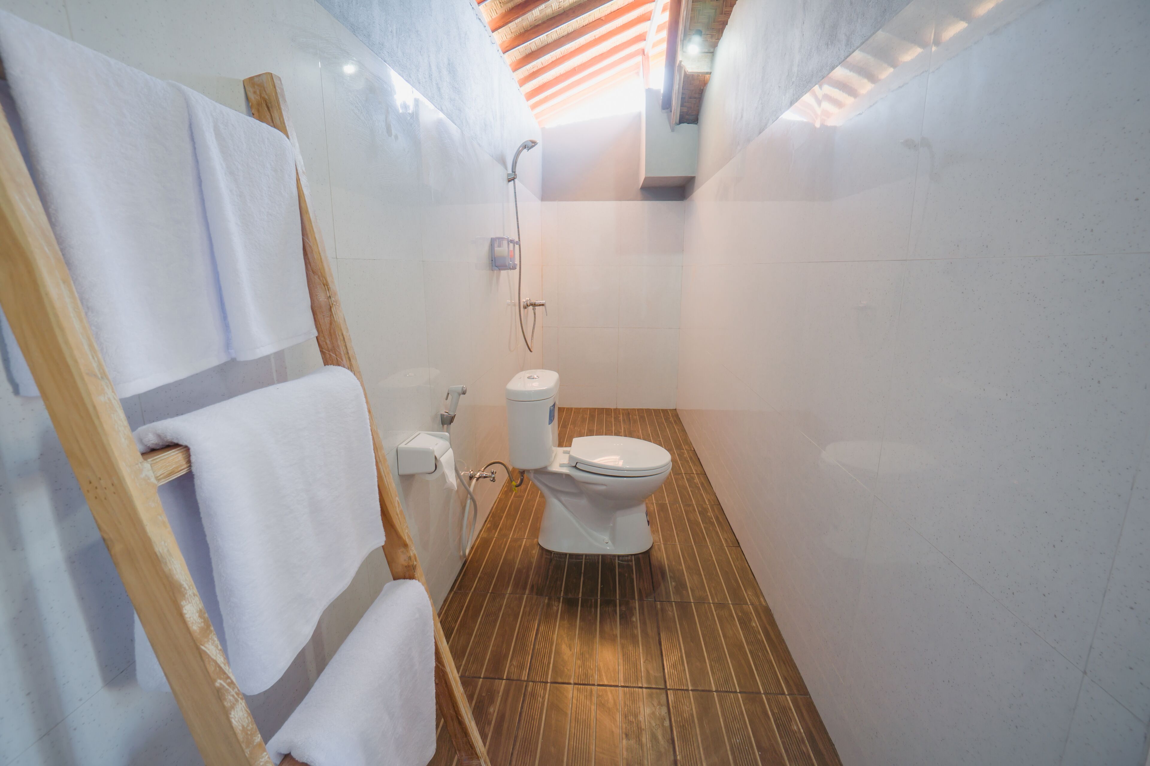 Un baño con piso de madera, paredes blancas, un inodoro blanco y una ducha.