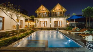 A two-story building with a swimming pool, outdoor seating, and a well-lit entrance. - Pi Karya Beach (Penida Island)