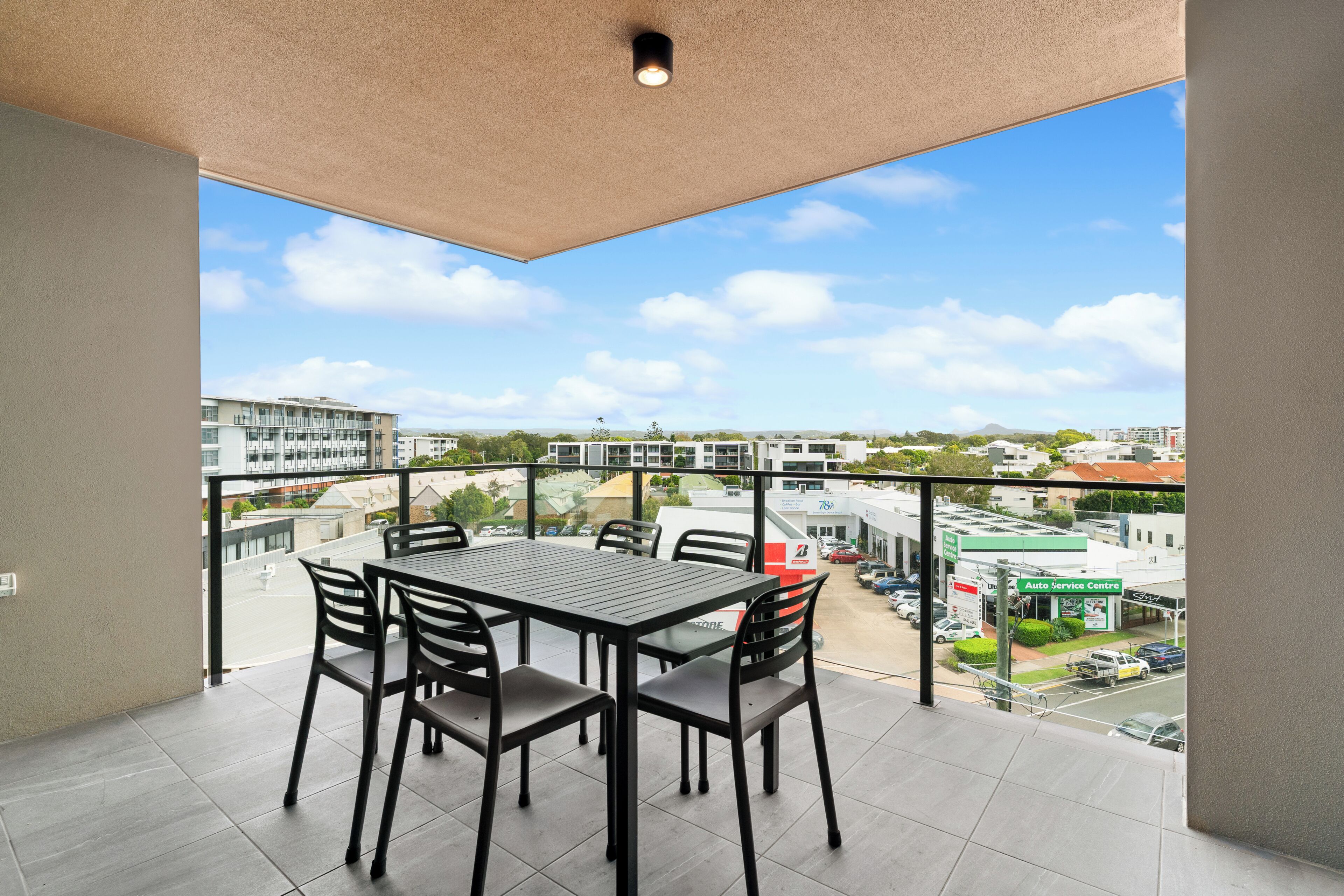 A balcony with a table and chairs, overlooking a street with buildings and cars.