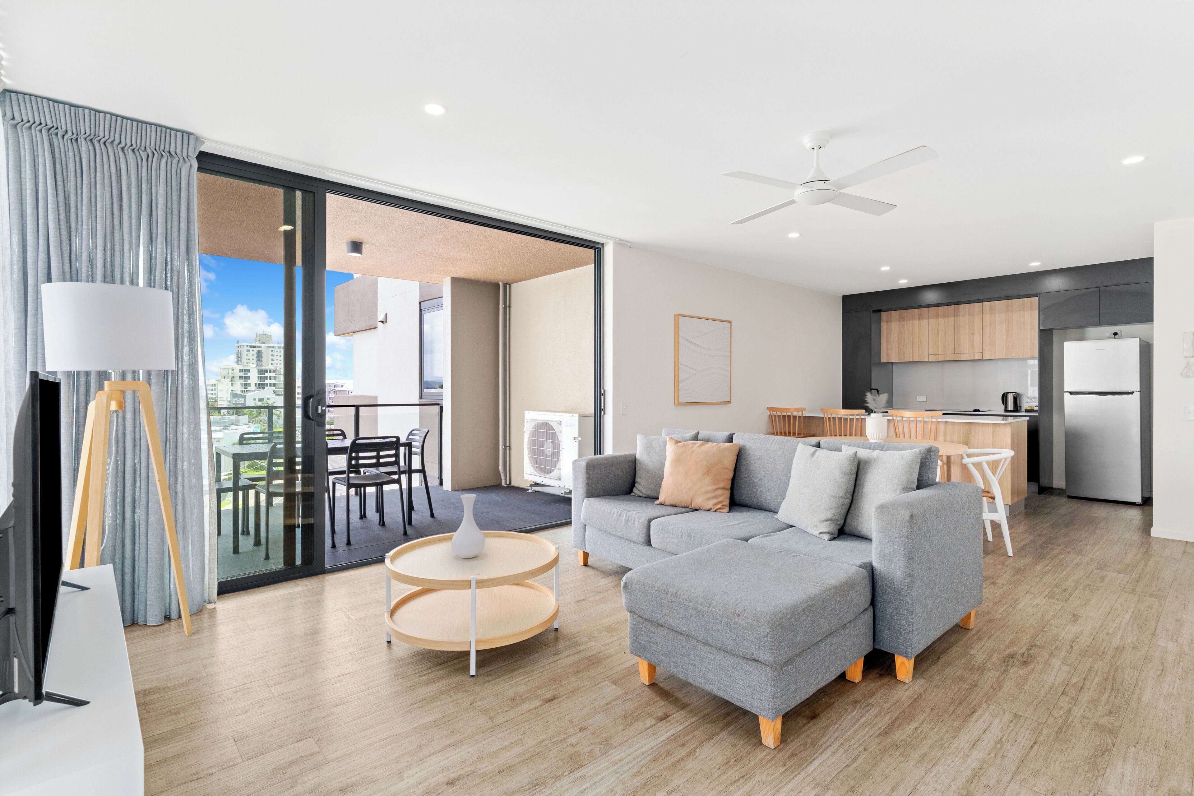 A modern living room with a grey sectional sofa, a round coffee table, and a dining area with a white table and chairs.