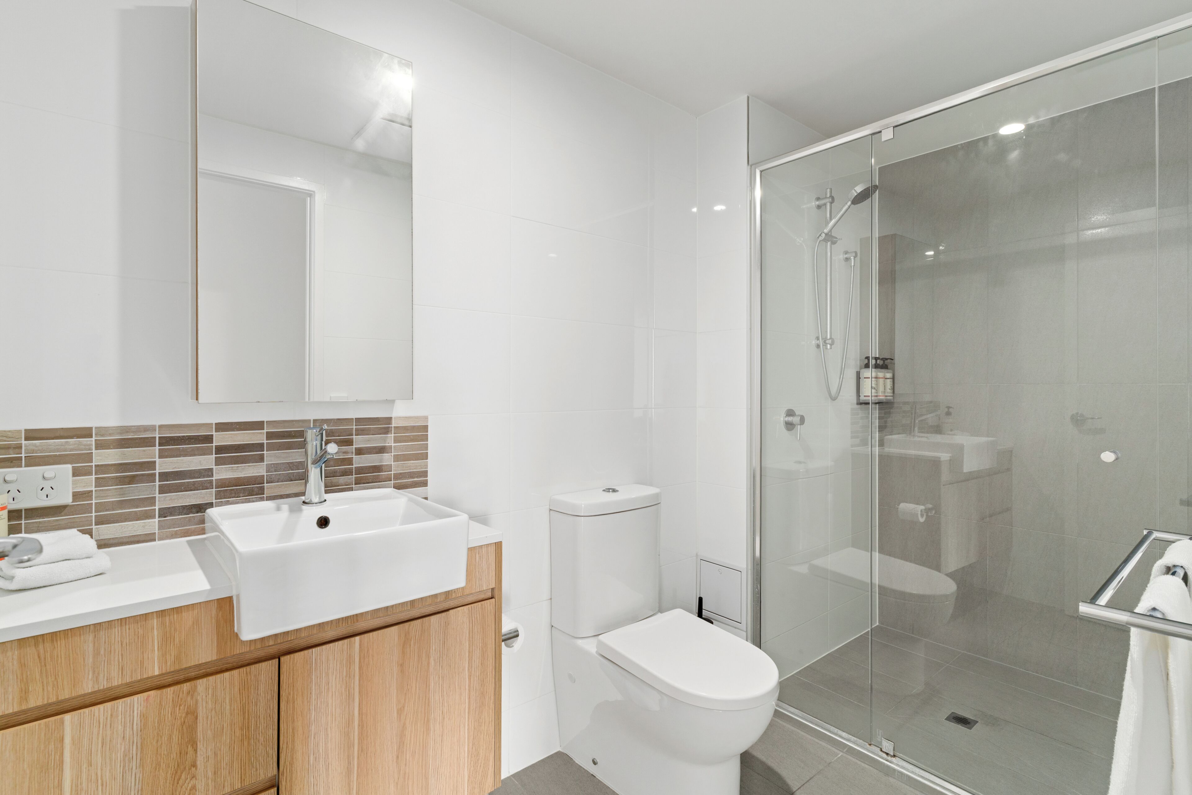 A modern bathroom with a glass-enclosed shower, a white sink, and a wooden vanity.