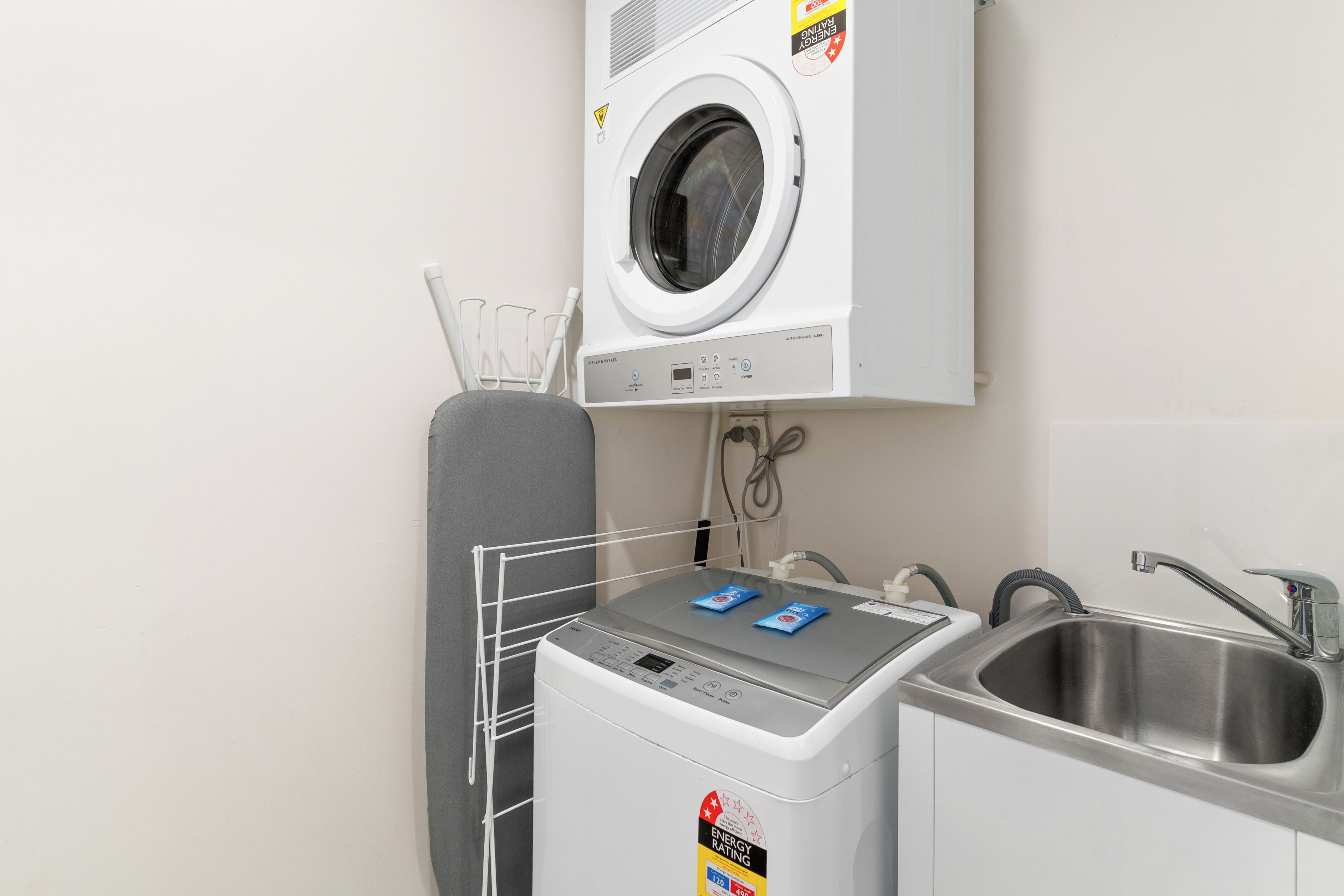 A compact laundry area with a washing machine, a drying rack, and a sink.