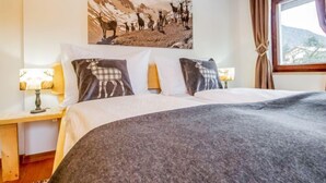 Een slaapkamer met een bed, twee nachtkastjes, een raam met gordijnen en een schilderij van herten aan de muur.