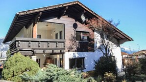 Een chalet met twee verdiepingen, een balkon, grote ramen en een berg op de achtergrond.