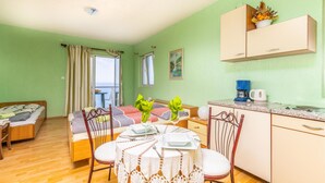 A room with a bed, a dining table set for two, a kitchen area, and a view of the sea through a window. - Nice apartment in Stara Baska with WiFi (Stara Baska)
