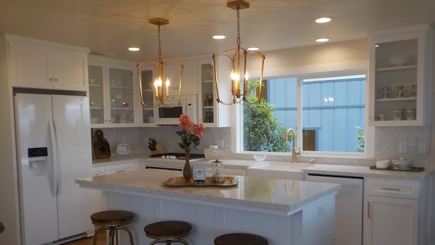 A modern kitchen with white cabinetry, a central island with stools, a chandelier, and a view of the outdoors. - Perfect Pink Paradise (Cayucos)