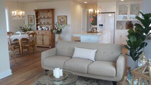 A living room with a sofa, a glass coffee table, and a dining area with wooden chairs and a cabinet. - Perfect Pink Paradise (Cayucos)