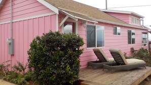 A pink house with a porch, two wicker chairs, and a small garden. - Perfect Pink Paradise (Cayucos)