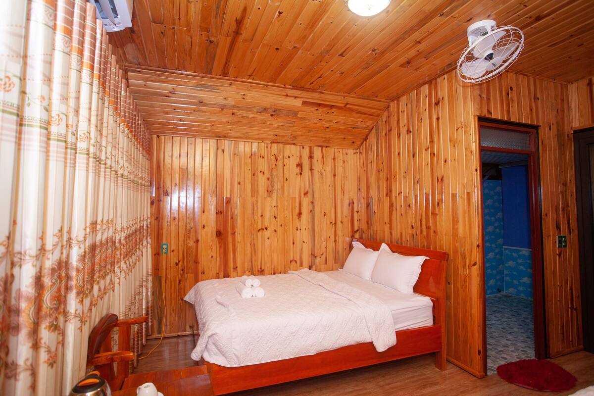Una habitación con paneles de madera, una cama, un ventilador y una zona de ducha.
