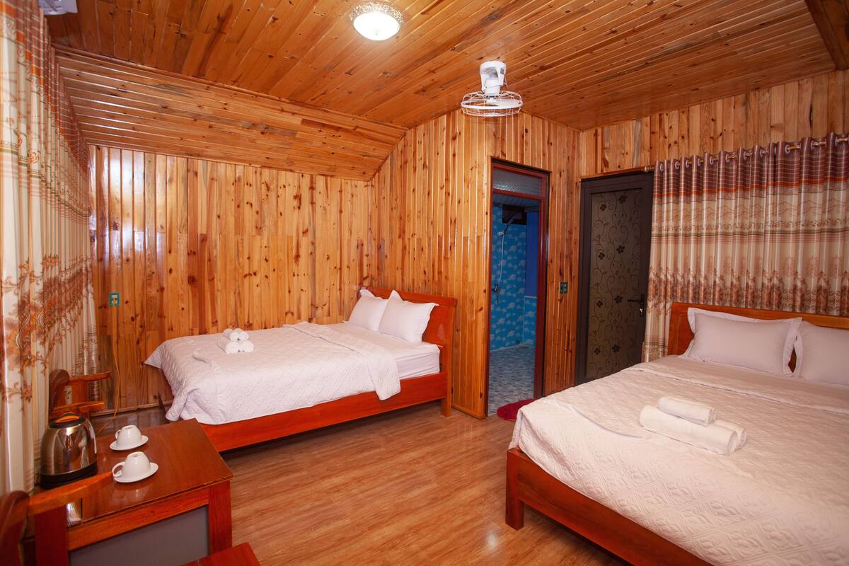 Una habitación con paneles de madera, dos camas, un escritorio de madera y un ventilador de techo.