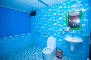 Een badkamer met een vloer van blauwe tegels, een wit toilet, een wastafel en een douchehoek.