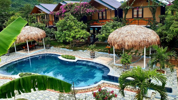 Een resort met een zwembad, rieten parasols en weelderig groen.