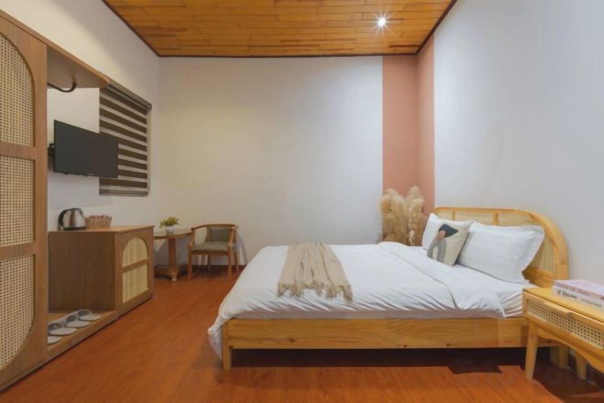 A bedroom with a wooden bed, a desk, a chair, and a TV on the wall.