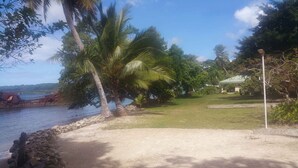 A coastal area with a grassy path, palm trees, and a building with a green roof. - Santo Seaside Villas (Luganville)