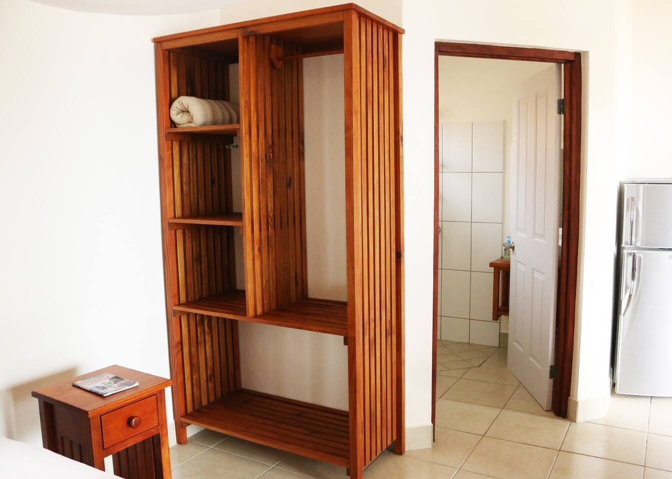 Una habitación con un armario de madera, una pequeña mesa de madera con una revista y un refrigerador blanco.