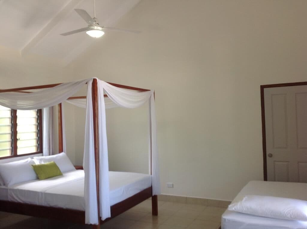 A bedroom with a four-poster bed, a single bed, a ceiling fan, and a door.