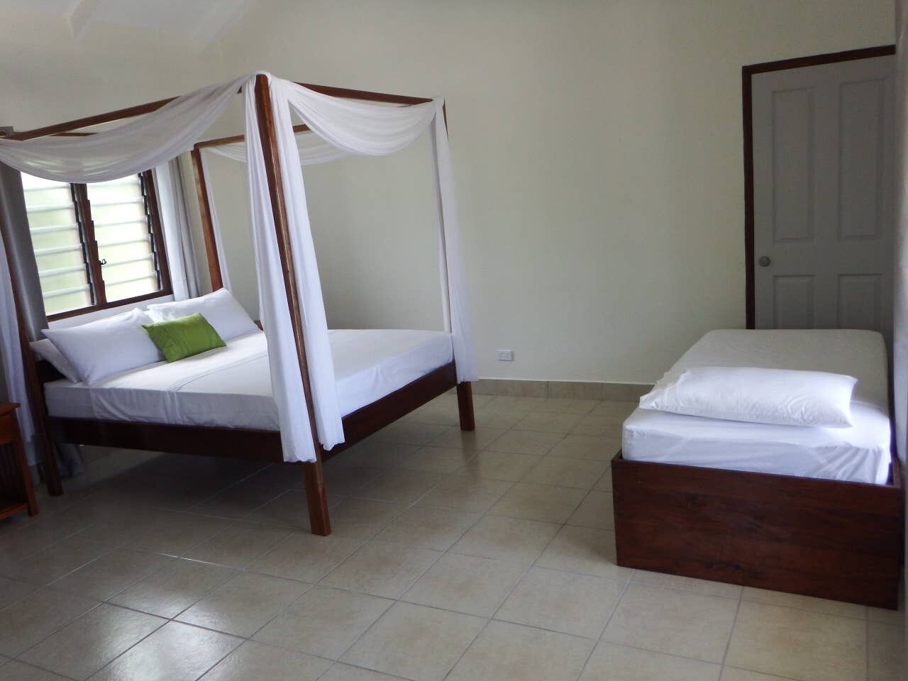 Quarto com cama de dossel e uma cama simples, ambas com roupa de cama branca.
