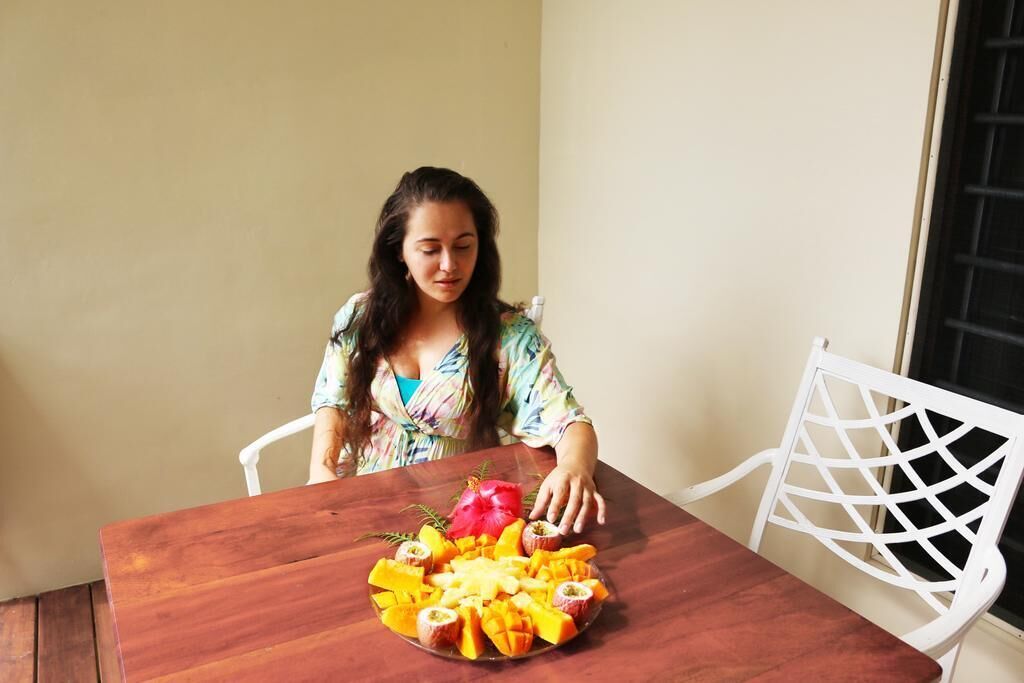 Una persona sentada a una mesa de madera con una bandeja de frutas frente a ella.