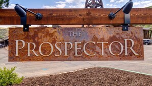 Een robuust metalen bord met de tekst 'THE PROSPECTOR' bevestigd aan een houten balk.