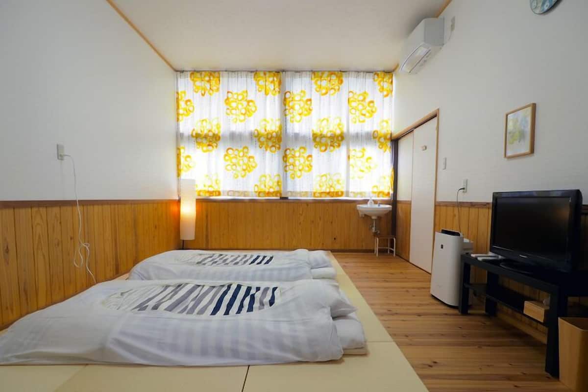 A room with two beds, a TV, a sink, and a window with patterned curtains.