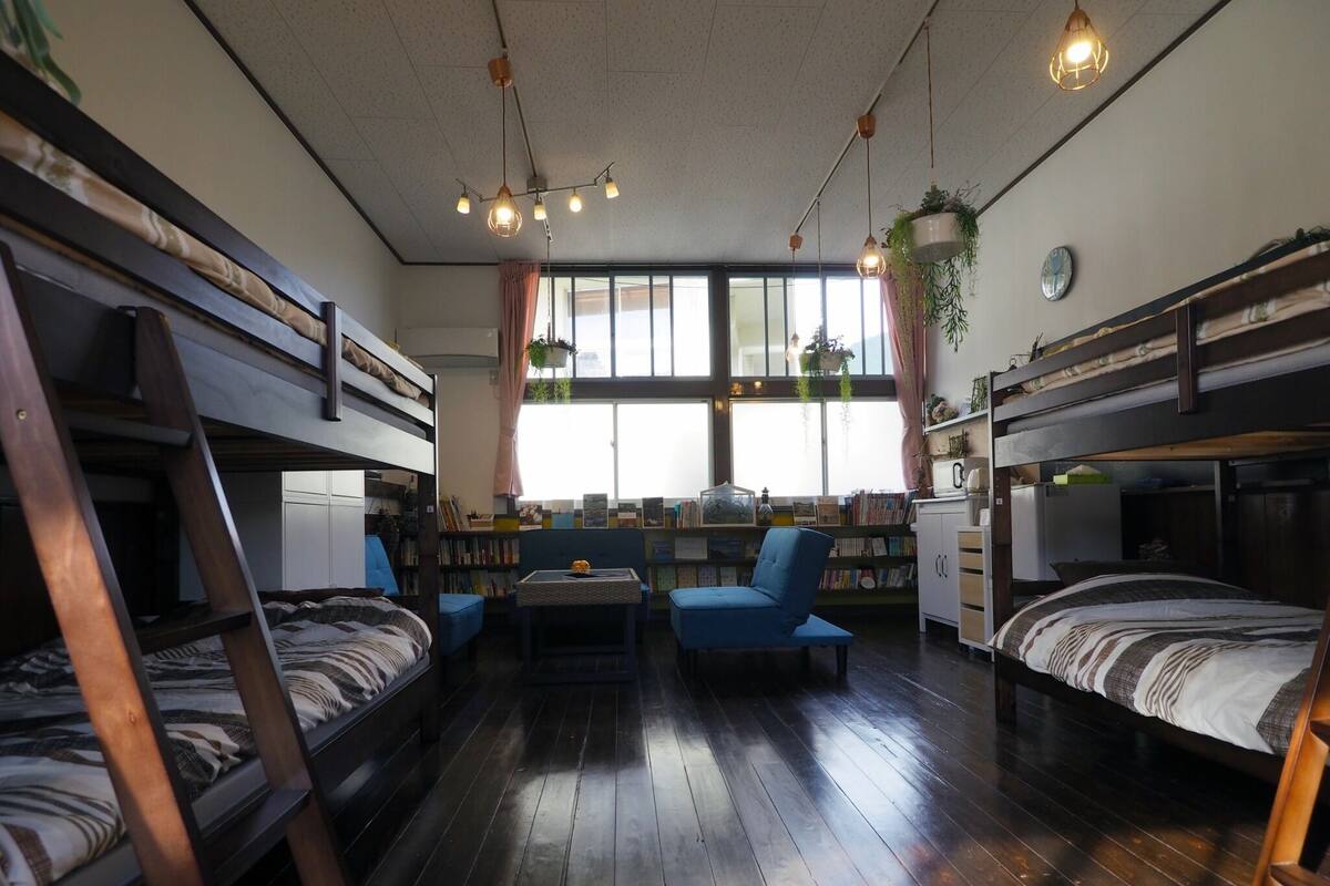 A room with bunk beds, a small table, a blue chair, and a bookshelf.