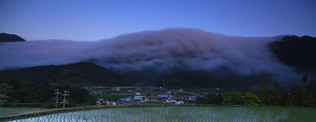 A rural landscape with a village, mountains, and a field.