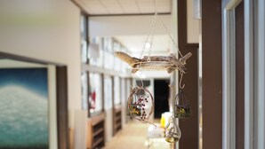A hallway with a wooden floor, a painting on the wall, and a hanging decoration with a birdcage and a glass ornament. - Mikan Hotel (Mihama)