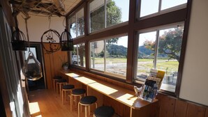 A restaurant with wooden tables and stools, large windows with a view of the outdoors, and hanging decorations. - Mikan Hotel (Mihama)