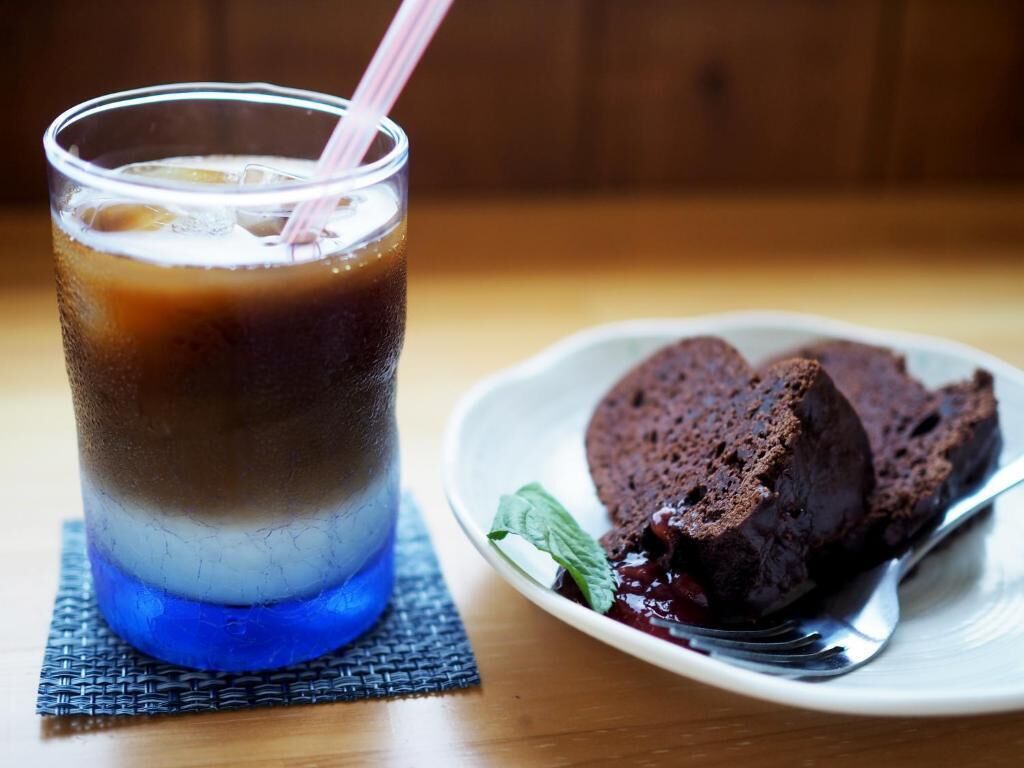 A glass of iced coffee with a straw and a plate of chocolate cake with berries.