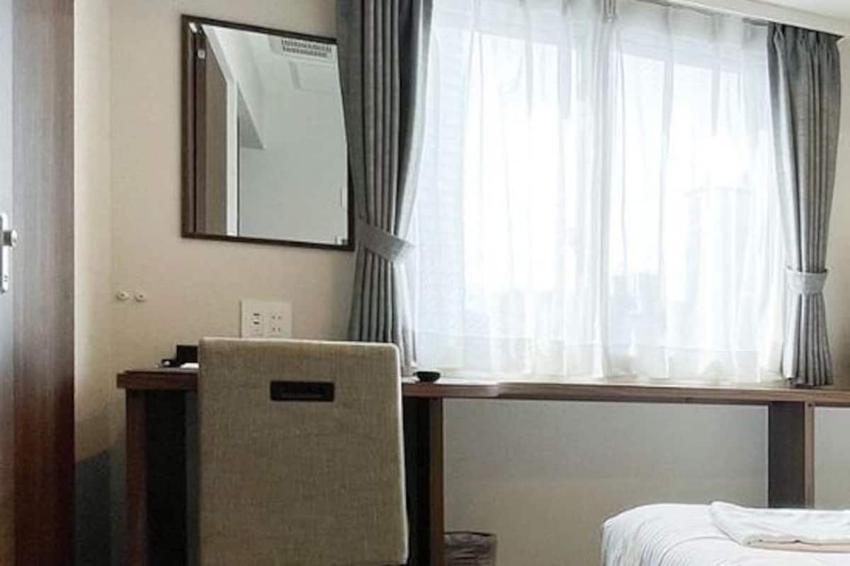 A hotel room with a bed, a desk with a chair, a television, and a window with curtains.