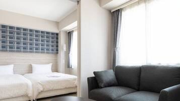 A hotel room with two beds, a sofa, a large window with curtains, and a wall-mounted TV.