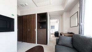 A modern hotel room with a grey sofa, a wooden wardrobe, a desk, and a large mirror. - Hotel Classe Stay Sapporo (Sapporo)