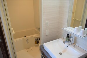 A bathroom with a bathtub, a sink, and a mirror. There are toiletries on the wall and a shelf with cups. - Hotel Classe Stay Sapporo (Sapporo)