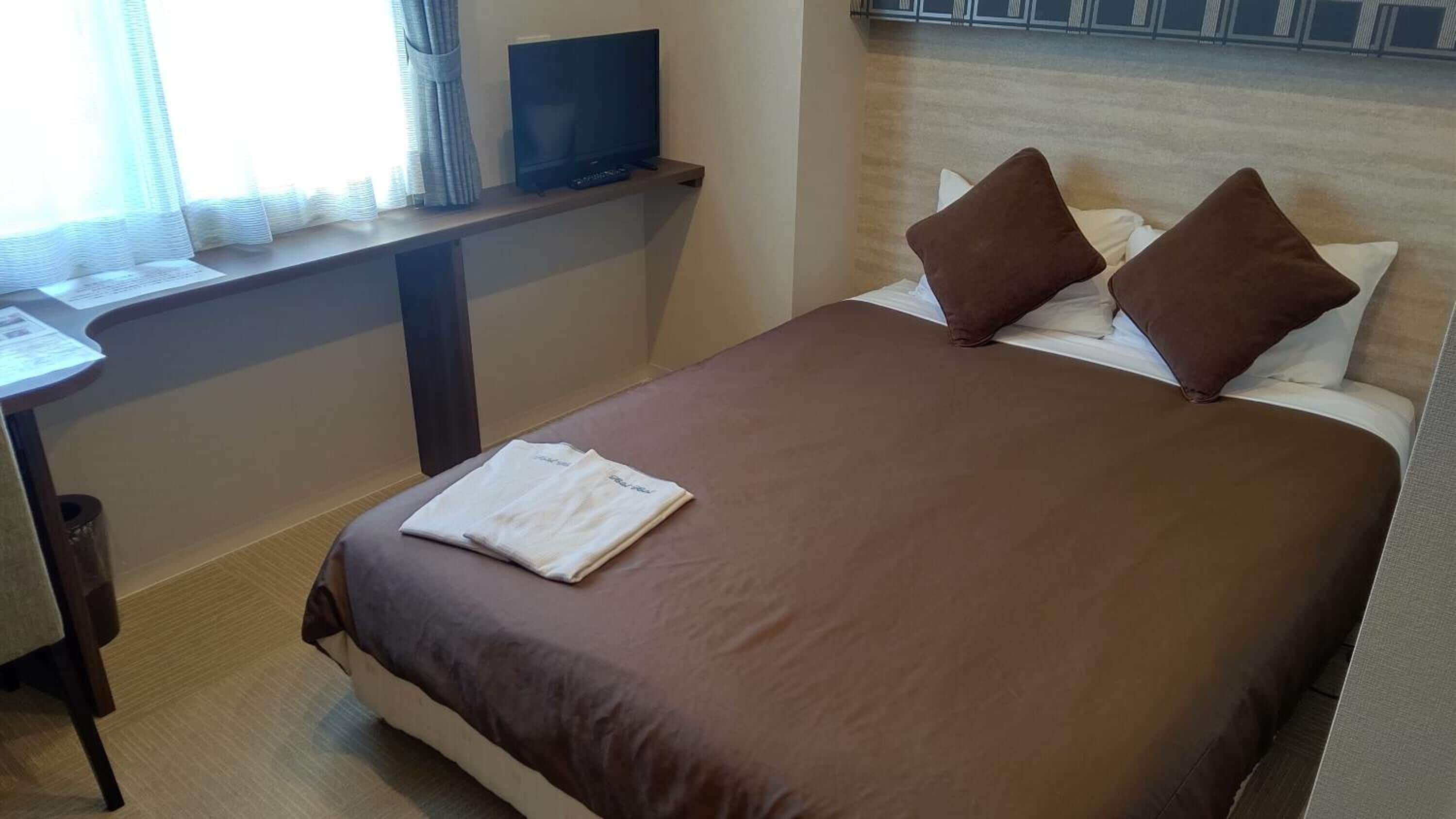 Ein Hotelzimmer mit Bett, Kissen, einem Fernseher auf einem Regal und einem Schreibtisch mit Stuhl.