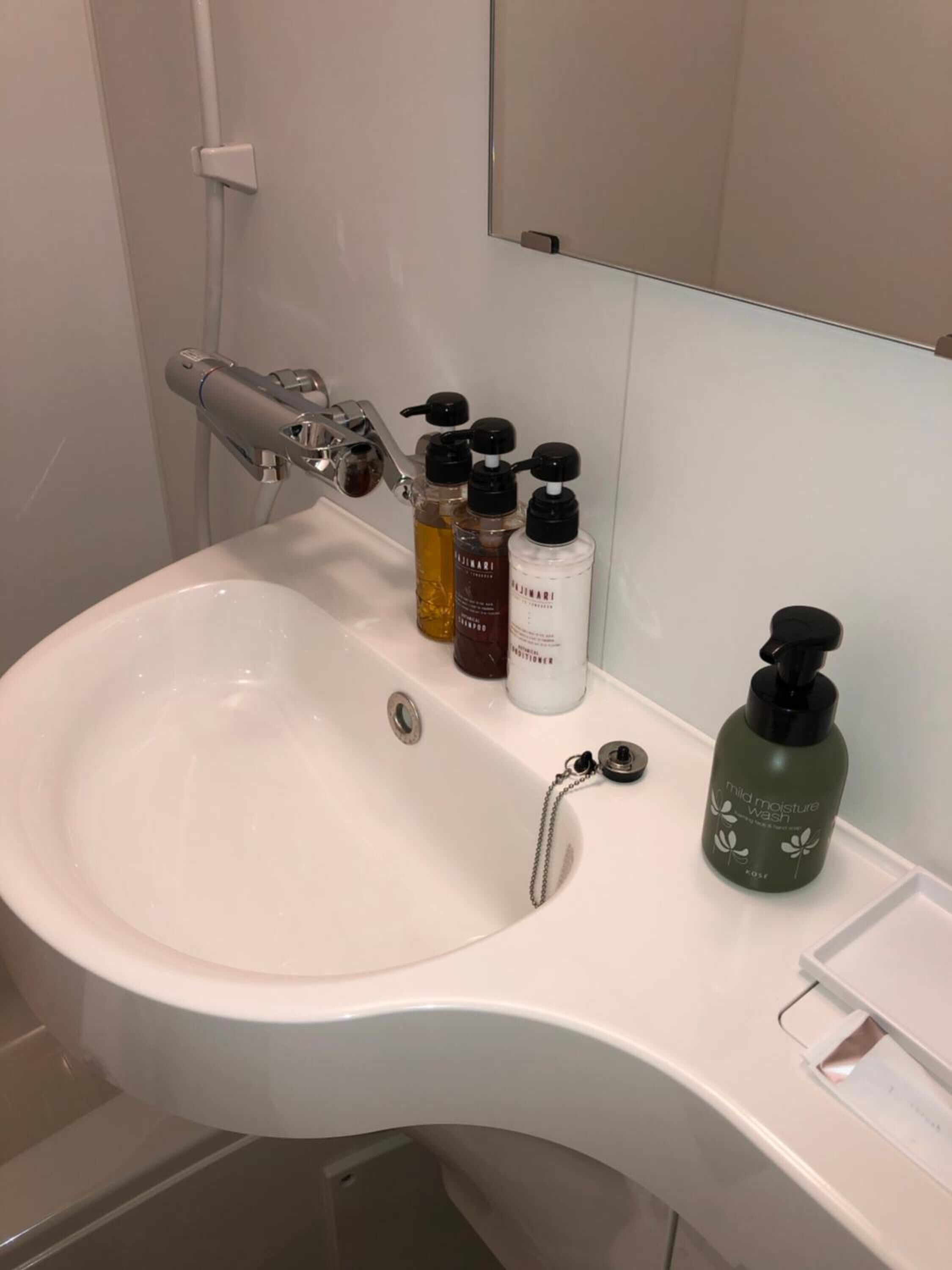 A white bathroom sink with a modern faucet, a mirror above, and three toiletry bottles on the counter.