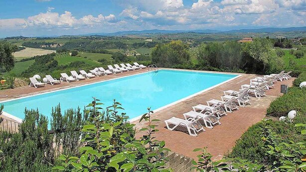 A swimming pool with lounge chairs, surrounded by greenery and a view of distant hills. - Holiday apartment with pool and terrace (Asciano)