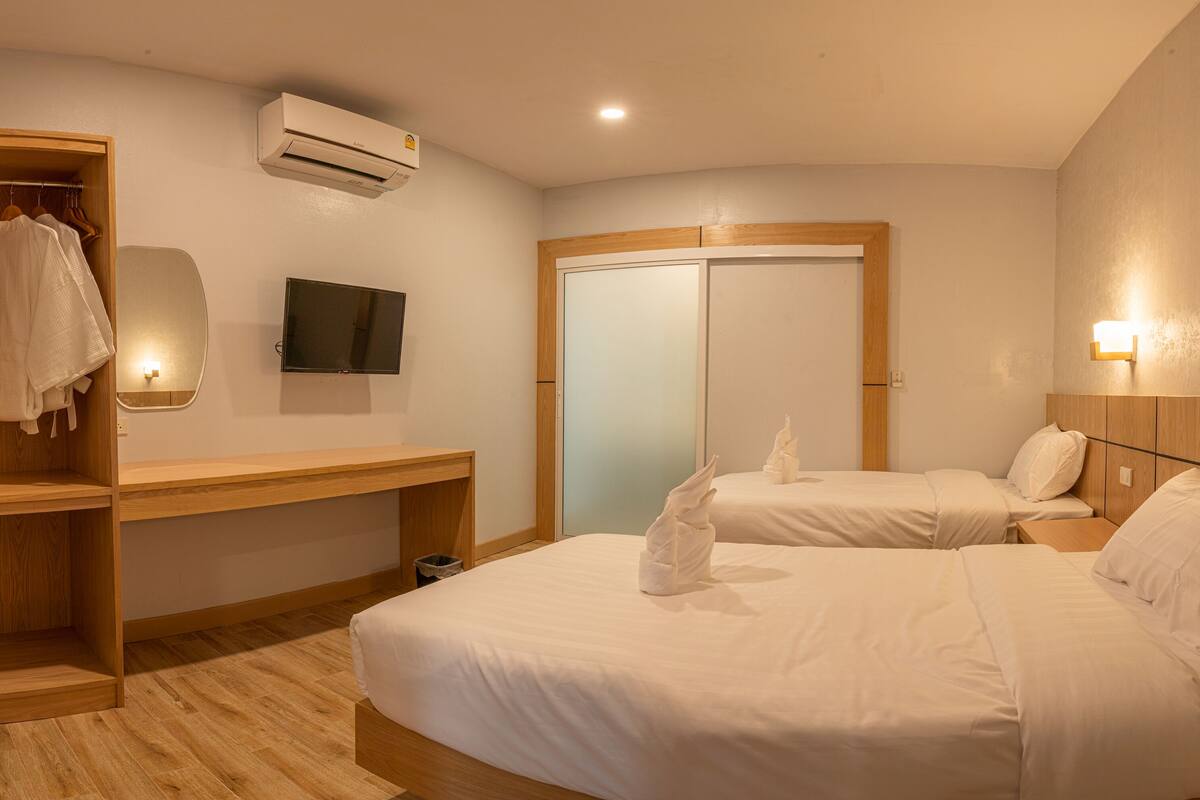 A hotel room with two beds, a wooden desk, a TV, an air conditioner, and a wardrobe.