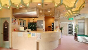 A reception desk with a curved design, a green door, and a potted plant. - Sauna Capsule Hotel Core 21 - Caters to Men (Tokyo)
