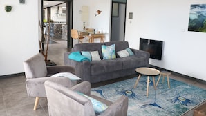 Een moderne woonkamer met een grijze bank, twee fauteuils, een ronde salontafel en een vloerkleed met pauwenmotief.