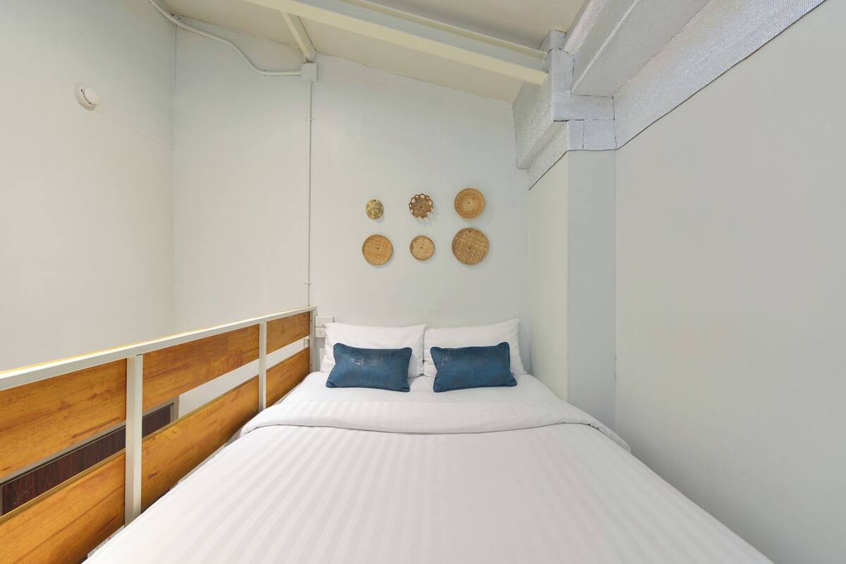 A bedroom with a wooden headboard, a white bedspread, and a wall-mounted air conditioning unit.
