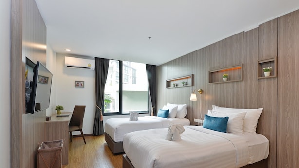 A hotel room with two beds, a desk, a chair, a TV, and a window with curtains. - StayAt Bedever Bangkok Hotel (Bangkok)