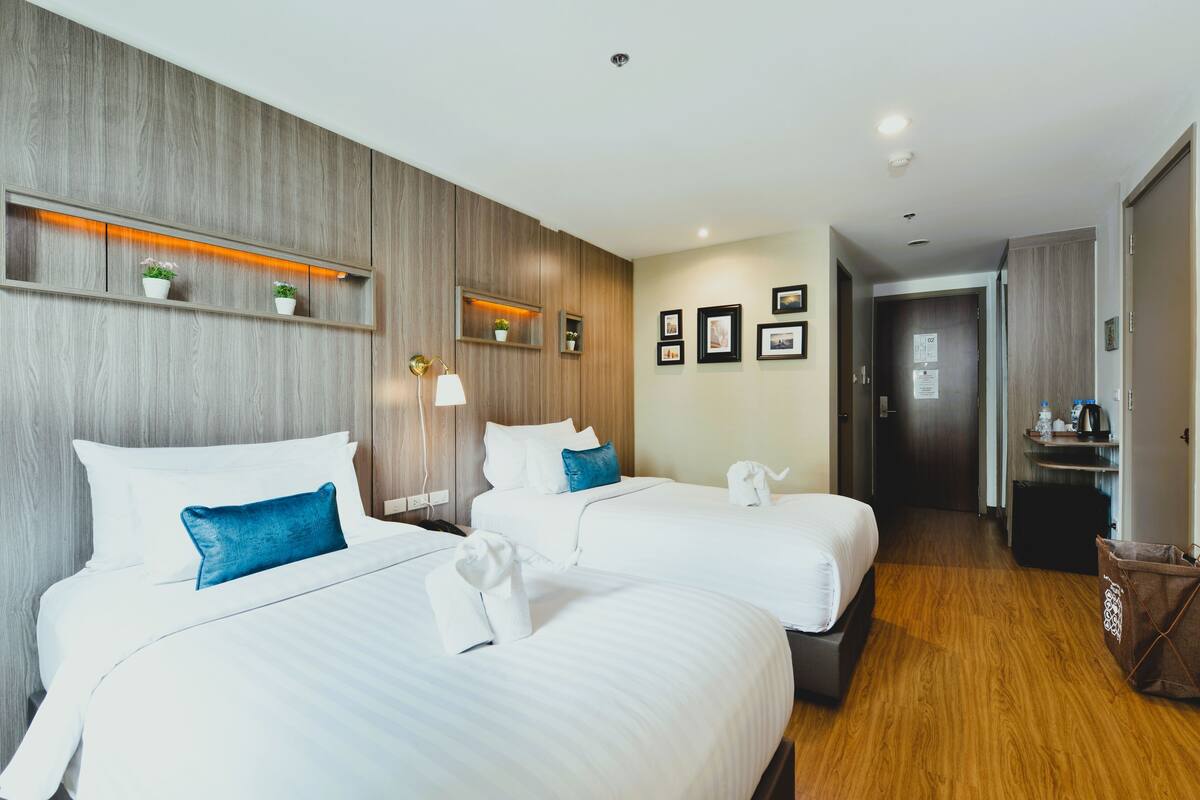 A hotel room with two beds, wooden paneling, a hallway, and a door.