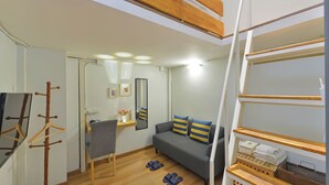 Un espacio habitable compacto con sofá, sillón, perchero y una mesita con espejo y objetos decorativos.