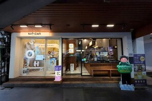 Entrada de hotel con un letrero que dice 'SLO CHA' y un anuncio del servicio 'GrabFood'.