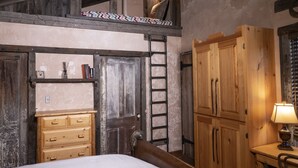 Un dormitorio rústico con cama estilo altillo, armario de madera y escalera de acceso al altillo.