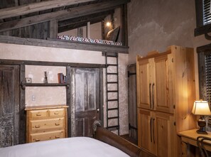 A rustic bedroom with a loft bed, wooden wardrobe, and a ladder leading to a loft space.