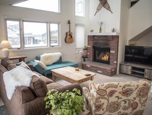 A living room with a sofa, a coffee table, a fireplace, a television, and a guitar. - Bright Mountain Retreat | Hot Tub | Bunk Room | 5 Baths | Sleeps 13 (Avon)