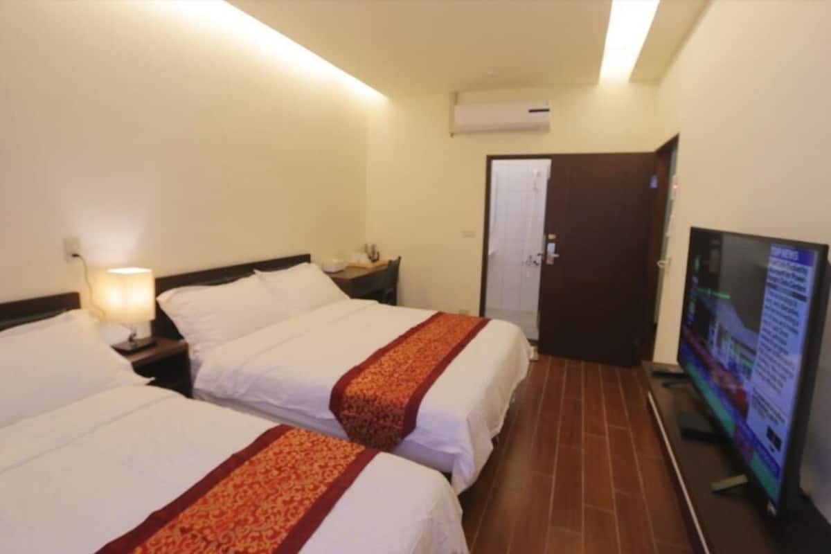 A hotel room with two beds, a TV, and an air conditioning unit.