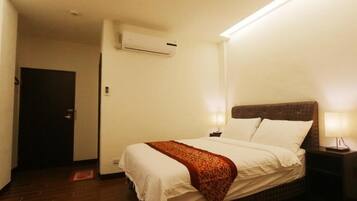 A hotel room with a bed, bedside lamps, an air conditioning unit, and a door.